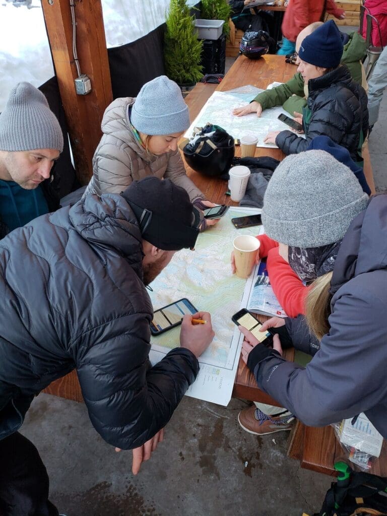 a group of students on an avalanche course plan out their trip around a table using a topographic map