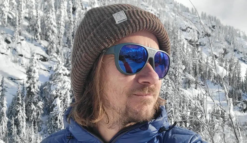 a man stands in front of a snowy mountain landscape wearing sunglasses for backcountry skiing