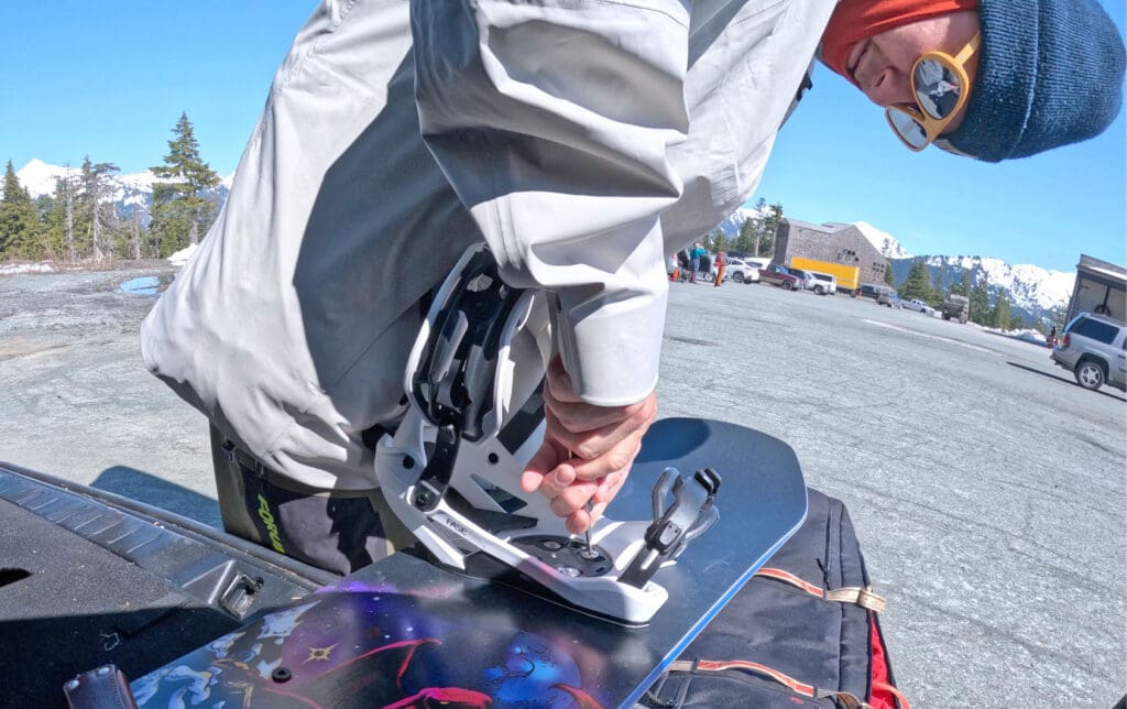 a snowboarder setting up his jones mercury fase bindings in. theparking lot of mount baker