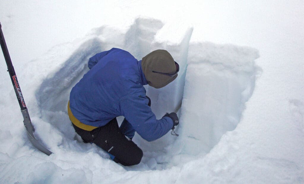 a man studies the snowpack structure inside a snow pit