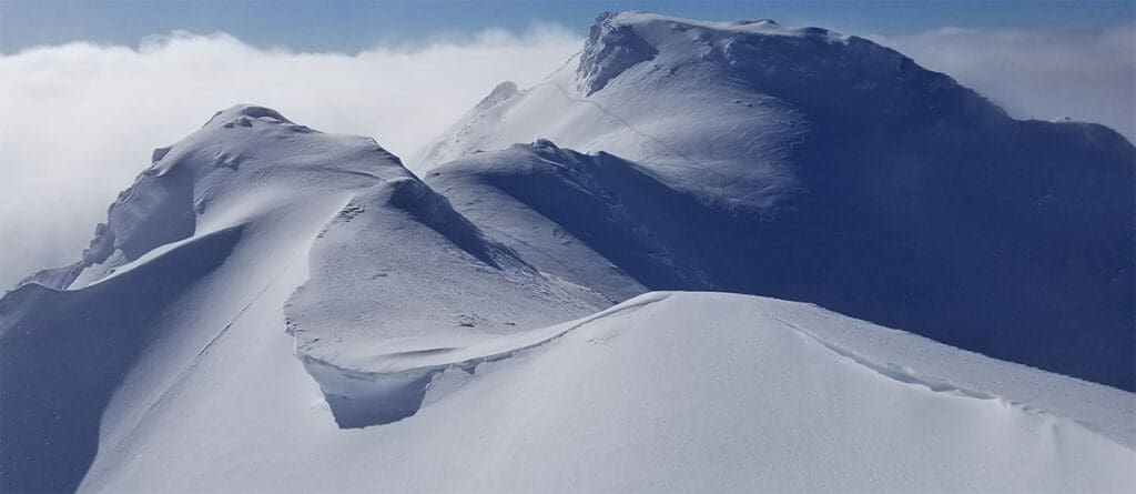 a snow covered mountain peak showing the effects of wind on a ridgetop.