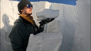 a snow science expert holds up some slabs from a compression test after digging a snow pit in the whistler backcountry