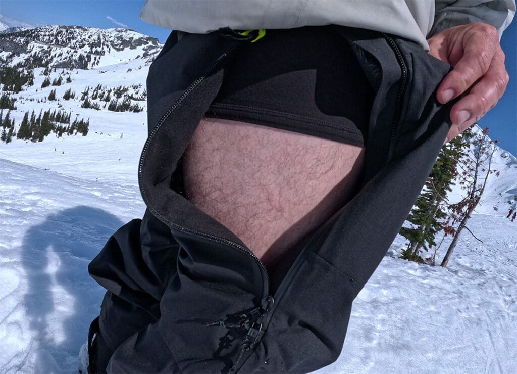 a snowboarder opens the side vents of his snowboard pants 