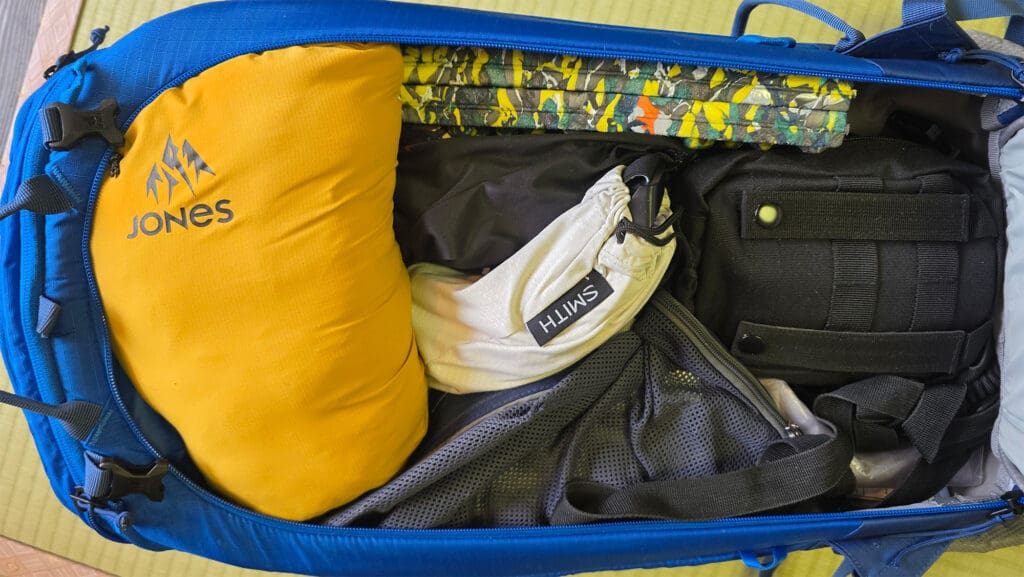 A backpack filled with contents needed for a day of backcountry skiing or splitboarding, including the jones dark start packed up