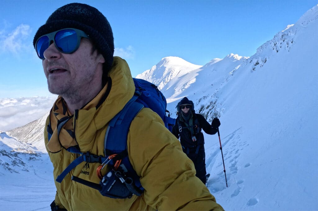 a par of backcountry snowboarders skinning up an alpine mountain