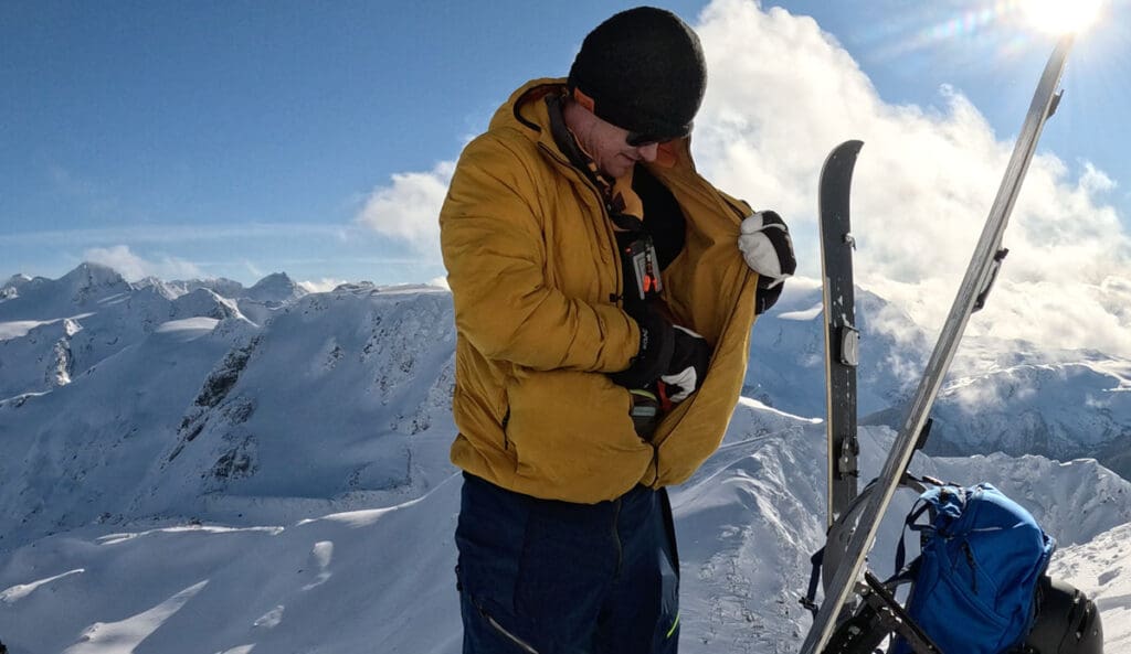a backcountry snowboarder puts skins on the inside of his puffy midlayer jacket