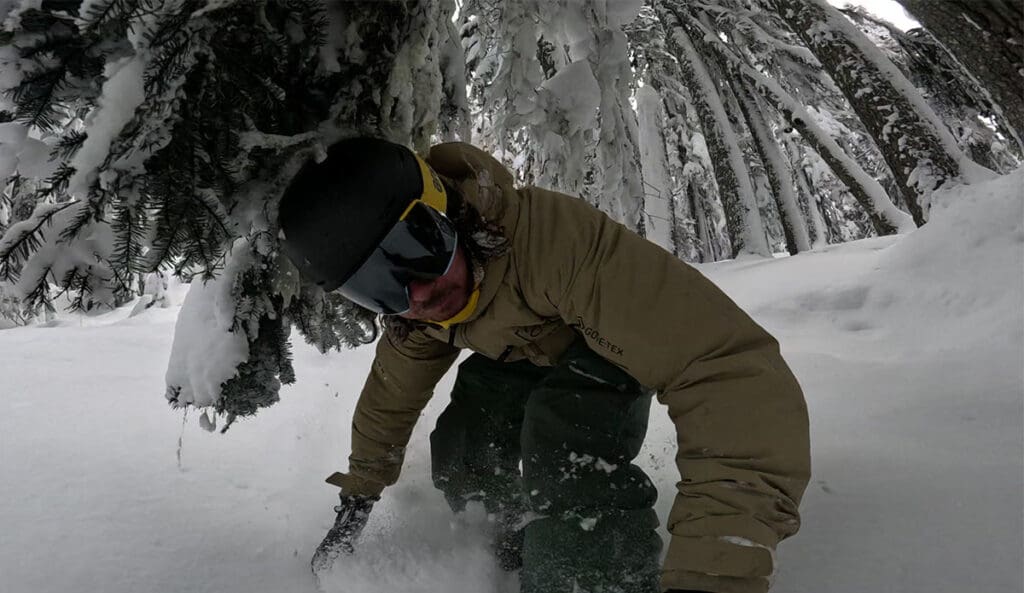 a snowboarder ducks under a tree while testing the anon merak helmet