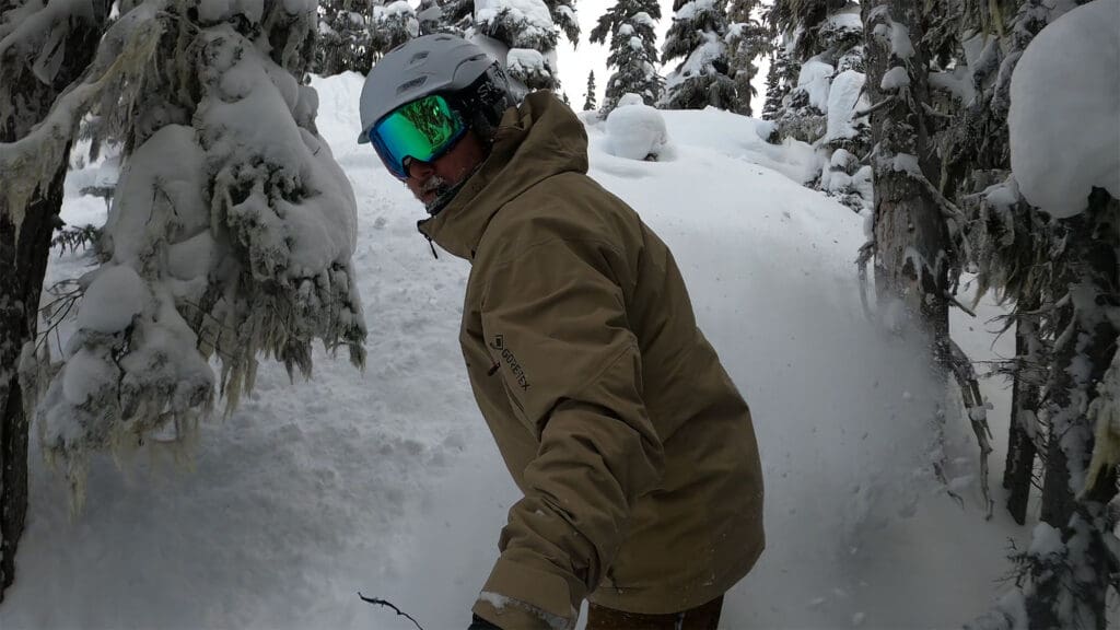 a snowboarder rides through the trees 