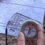 a close up photo of someone using a compass lined up on a topographic map