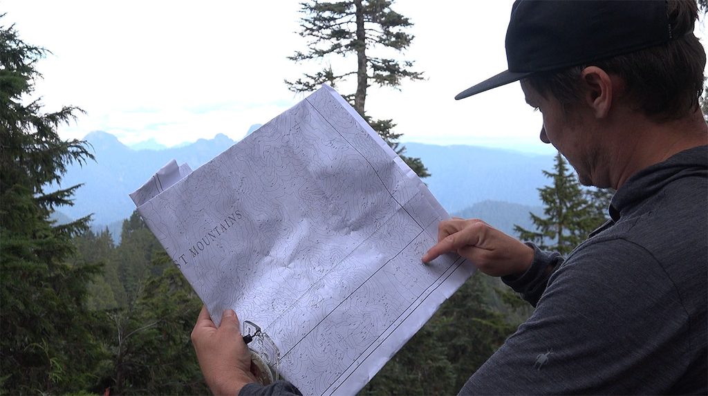 a man looks at a topographic map while trying to find his position in the coast mountains of British Columbia