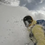 a snowboarder emerges from a cloud of powder in Japan