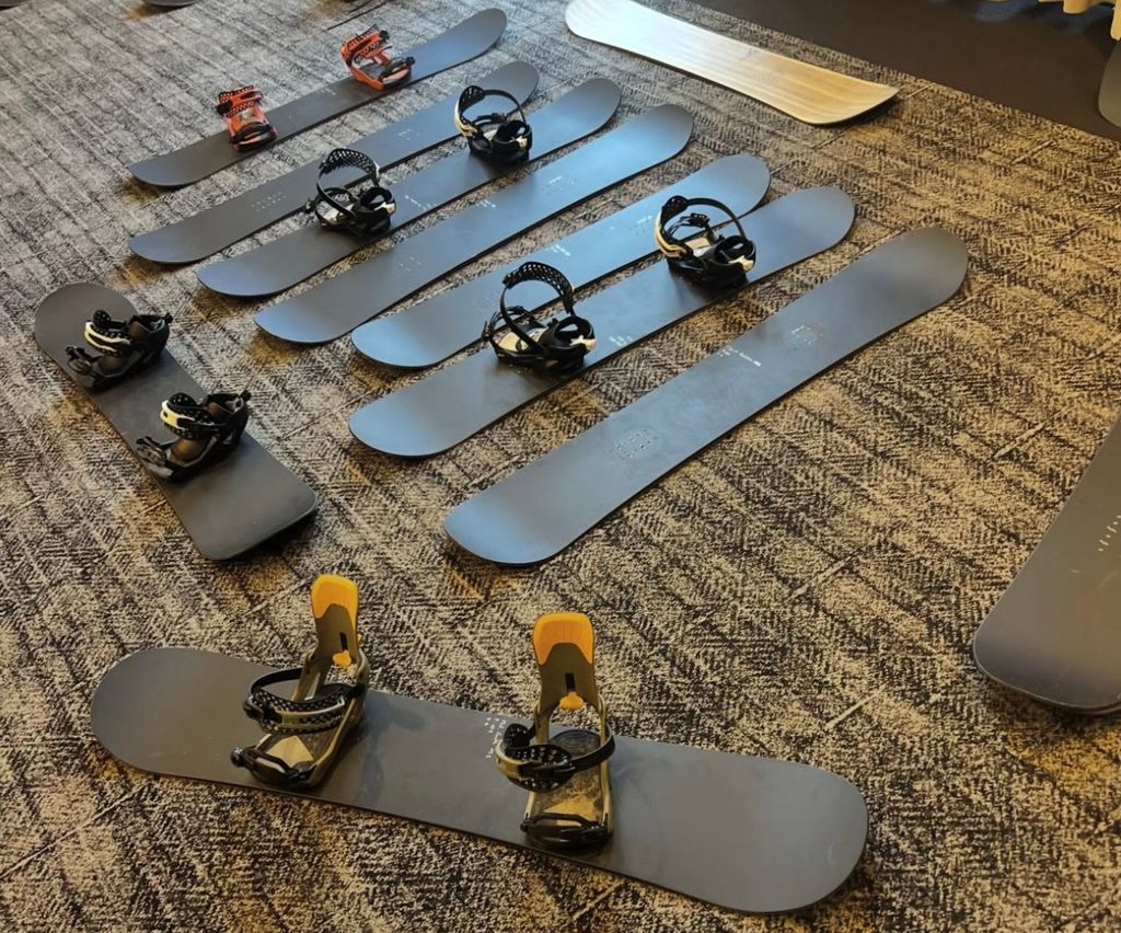 a collection of prototype snowboards with black topsheets on a hotel room floor
